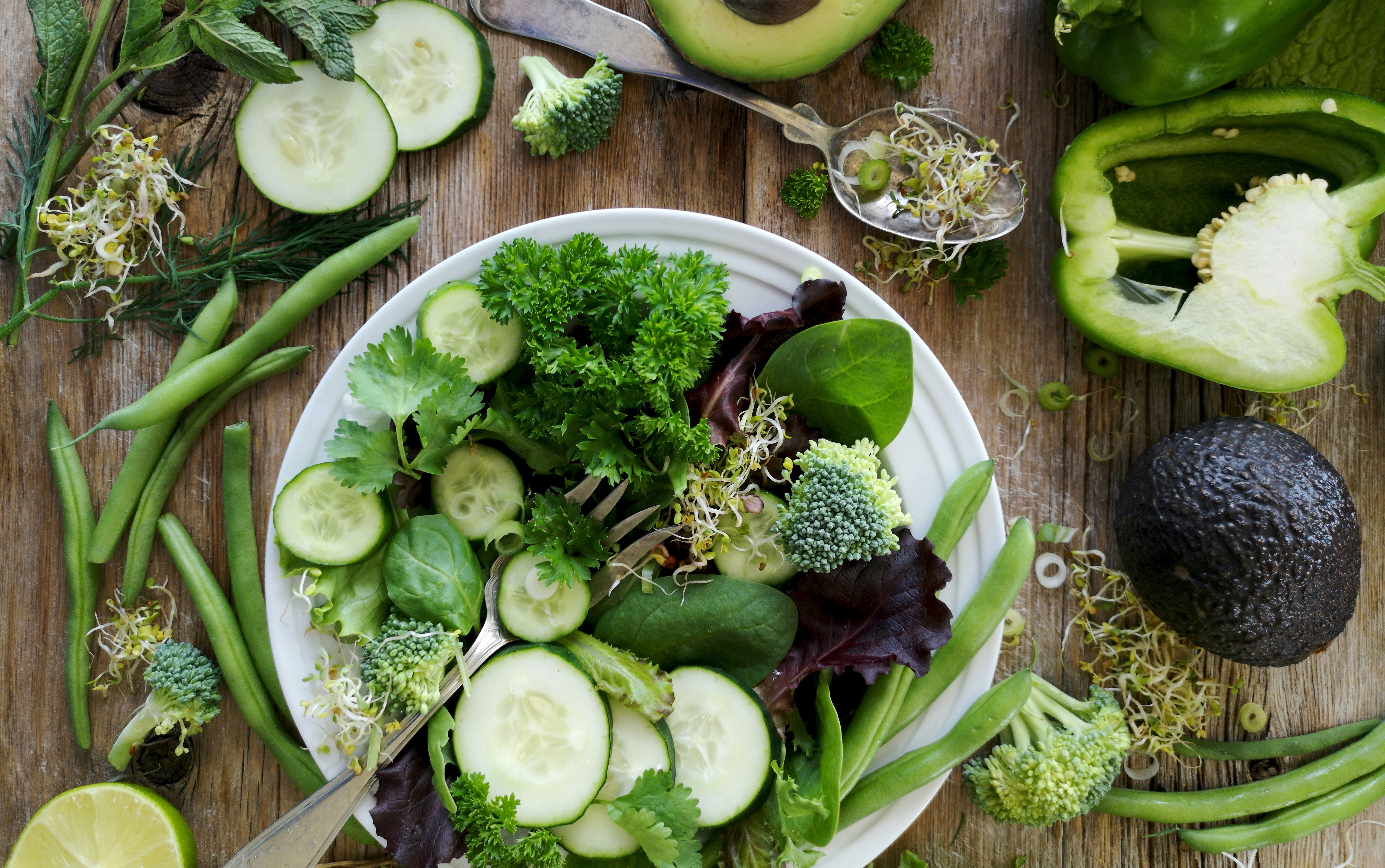 A plate of fresh greens surrounded by whole vegetables and herbs